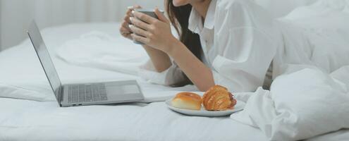 glücklich freiberuflich asiatisch Frau Arbeit auf Tablette auf das Hotel Bett auf Reise Reise. foto