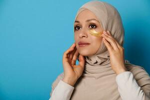 Nahansicht von Muslim Frau im Hijab mit Hydrogel Auge Flecken. Schönheit Porträt auf Blau Hintergrund mit Kopieren Raum foto