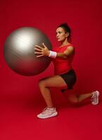 attraktiv sportlich Frau tun nach vorne Ausfallschritte während ausüben mit ein passen Ball, halten es beim Truhe eben, isoliert Über rot Hintergrund mit Kopieren Anzeige Raum foto