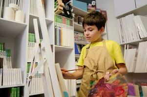 süß Teen Junge suchen zum Inspiration, zeichnet auf Leinwand, Lernen fein Kunst Gemälde im Werkstatt. Hobbys und Freizeit foto