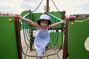ein süß wenig Mädchen klettert das Seile beim das Spielplatz beim das Kinder- Sommer- Lager. aktiv während das Sommer- Ferien foto