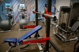 Fotos von das Innere von das Fitnessstudio mit ein Bank Drücken Sie, ein Eisen Hantel, Hanteln, Gewichte und Übung Maschinen.