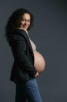 herrlich schwanger Frau mit nackt Bauch, isoliert Über grau Studio Hintergrund. Schwangerschaft. Mutterschaft. gebärfähig foto