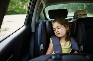 sicher Bewegung von Kinder im das Wagen. wenig Mädchen schläft im ein Booster Sitz im das Wagen. Kind Sicherheit Sitz. foto