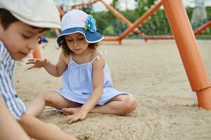 bezaubernd Kinder, Junge und Mädchen, spielen auf das sandig Spielplatz auf das Strand. Kindheit und Sommer- Ferien Konzepte. Sommer- Lager foto