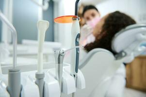 Fokus auf modern Dental Ausrüstung benutzt im Dental trainieren auf das Hintergrund von verschwommen Zahnarzt mit modern Besondere ultraviolett Licht Lampe zum Zähne Bleaching Verfahren. foto