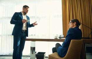 müde Geschäft Frau Hören zu das Erklärungen von ihr Mitarbeiter, Wer ist Stehen Nächster zu das Tabelle mit ein Tasse von Kaffee im Hand. gut aussehend Mitte alt haben ernst Diskussion mit seine weiblich Boss foto