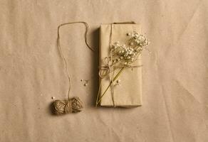 eben legen Frühling Komposition mit Weiß Gypsophila Zweig auf Geschenk Box im Kraft Verpackung Papier und gebunden Seil Bogen auf zerknittert Karton Hintergrund mit Kopieren Raum zum Werbung foto