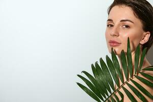 horizontal Nahansicht von ein wunderbar attraktiv Herrlich nackt Frau mit exotisch Palme Blatt, posieren auf Weiß Hintergrund mit Kopieren Raum. Konzept von mit natürlich organisch Kosmetika zum Haut Pflege foto