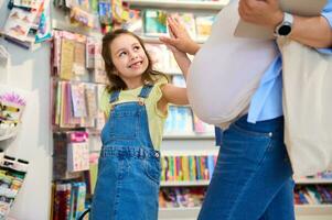 heiter lächelnd Kind Mädchen gibt hoch fünf zu ihr Mutter während Einkaufen zusammen zum Schule liefert im Schreibwaren Geschäft foto