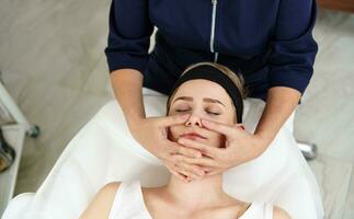 oben Aussicht von Kosmetikerin tun Gesichts- Antialterung Heben Massage auf Frau Gesicht beim Spa Klinik. Fachmann lymphatisch Drainage Massage beim modern Spa Center foto