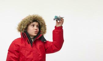 Nahansicht Porträt von ein bezaubernd Schule Junge spielen mit ein Flugzeug Spielzeug Modell, imitieren das Flug im das Himmel. isoliert Über Weiß Hintergrund. Winter Ferien Reise Konzept mit Kopieren Anzeige Raum foto