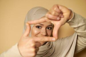 Nahansicht von ein attraktiv aussehen von schön arabisch Muslim Frau im Hijab durch Finger Frames foto