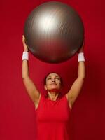 Porträt von ein Fitness glücklich passen Frau Stehen halten ein passen Ball im ihr angehoben Waffen über ihr Kopf. Kopieren kostenlos Raum zum Text. foto