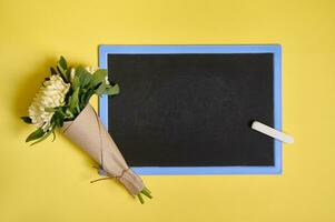eben legen Komposition von zart schön stilvoll Strauß von Astern Blumen im Kunst Verpackung Papier gebunden mit ein Seil auf ein leer leeren Tafel mit Raum zum Text isoliert auf Gelb Hintergrund foto