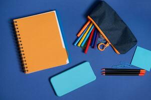 Schule Büro liefert und ein Smartphone Lügen Bildschirm Nieder auf ein Blau Hintergrund . eben legen Komposition von Schreibwaren im zwei kontrastieren Farben, Blau und Orange mit Kopieren Raum foto