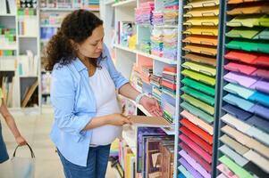 attraktiv schwanger Frau wählen Farbe Papier zum Design, Pastell- Zeichnung oder Aquarell Gemälde im Kunst stationär Geschäft foto