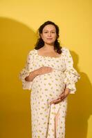 charmant schwanger Frau im Weiß Sommer- Sommerkleid, streicheln ihr Bauch im das neunte Monat von glücklich sorglos Schwangerschaft foto