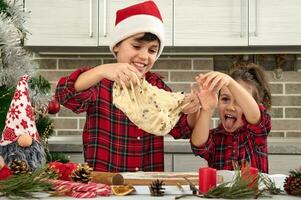 schön Kinder Kochen zusammen im das Zuhause Küche während Weihnachten Feiertage. bezaubernd Junge im Santa Hut und seine süß wenig Schwester vorbereiten und kneten Teig zum Brot foto