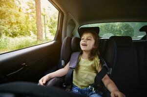 glücklich Mädchen im ein Kind Auto Sitz tragen ein Sicherheitsgurt während Reisen durch Auto foto