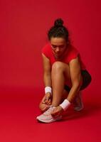 Sportlerin, Athlet, Läufer im Activewear binden Schnürsenkel auf Turnschuhe Vor Betrieb, isoliert auf rot Hintergrund mit Kopieren Anzeige Raum foto