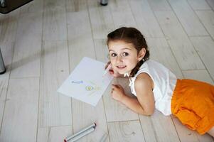 Overhead Aussicht schön Vorschulkind Mädchen Zeichnung Bild mit Filzstifte, lächelnd süß suchen beim Kamera. Kinder. Hobby. foto