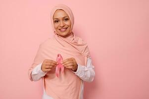 freundlich und solidarisch arabisch Muslim Frau im ein Rosa Hijab hält ein Rosa Band zu ihr Truhe Ebenen zum Brust Krebs Kampagne, fördern Krebs Bewusstsein. Rosa Oktober Monat , Damen Gesundheit Pflege Konzept foto