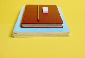 ein Gummi, Bleistift auf ein Buch mit Hardcover , Lehrbücher, isoliert auf Gelb Hintergrund mit Kopieren Raum foto