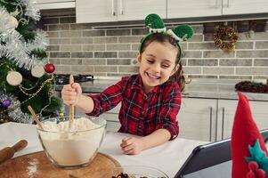 schön europäisch Kind, bezaubernd Mädchen mit Elf Band auf ihr Kopf , wenig Koch Blogger Mischen Zutaten im ein Glas Schüssel mit Mehl, vorbereiten Teig zum Weihnachten Kekse und Brot beim Zuhause Küche foto