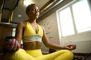 schön afrikanisch Frau tragen hell Gelb Trainingsanzug Sitzung im Lotus Position mit Augen geschlossen und meditieren. Yoga, Meditation, Achtsamkeit, Entspannung Übungen und aktiv Leben Stil Konzept foto