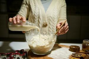 Nahansicht Frau Gießen Pflanze basierend Milch in ein Schüssel mit Mehl, zum vorbereiten Teig zum Weihnachten Lebkuchen Kekse foto