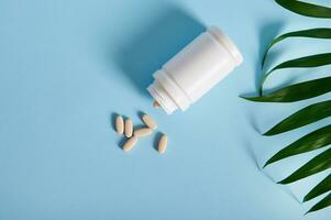 medizinisch Tabletten verstreut von ein Weiß Container in der Nähe von ein Palme verlassen auf ein Blau Hintergrund foto