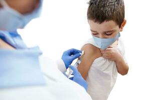 erschrocken Junge sieht aus beim seine Hand während Arzt Impfung ihn. isoliert auf ein Weiß Hintergrund foto