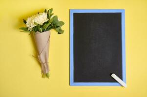 eben legen Komposition von ein zart Strauß von Herbst Astern Blumen im Kunst Verpackung Papier gebunden mit ein Seil und leer leeren Tafel mit Raum zum Text isoliert auf Gelb Hintergrund foto