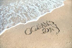 Inschrift des Ozeans Tag auf golden Sand durch das Meer. Sommer- Konzept foto