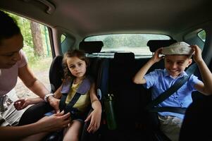 Mutter Befestigung ihr Tochter zu Kind Sicherheit Sitz Innerhalb Wagen. Kinder auf Sicherheit Booster Auto Sitz Innerhalb das Fahrzeug foto