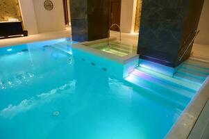 Aussicht von ein schön geräumig Innere mit Innen- Thermal- Schwimmen Schwimmbad mit Wasserfall im ein Luxus Salon Bereich von ein Wellness Spa Center foto