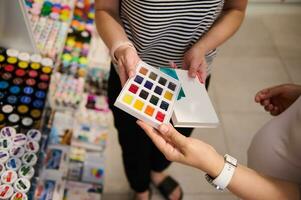 Nahansicht Hände von ein Verkäufer zeigen zu ein Kunde das schön Palette von beschwingt Aquarelle im kreativ Kunst Geschäft foto