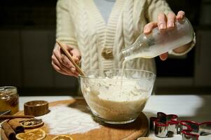 unkenntlich Frau vorbereiten Teig zum Weihnachten Lebkuchen Kekse, Gießen Milch in ein transparent Glas Schüssel mit Mehl foto