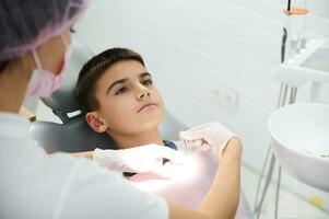 medizinisch Dental Assistent vorbereiten vorpubertär Schule Junge Lügen auf Zahnarzt Stuhl zu regulär medizinisch Untersuchung während Dental Termin. Konzept von Oral und Dental Gesundheit Pflege, pädiatrisch Zahnheilkunde foto