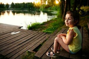ein charmant Mädchen ruhen auf das Seebrücke und suchen in das Entfernung gegen das Hintergrund von das Fluss Bank. Camping, Sommer- Themen. foto