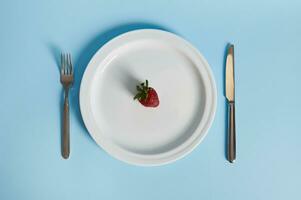 eben legen Komposition mit ein köstlich Erdbeere auf ein Platte, Gabel und Messer isoliert auf Blau Hintergrund. foto
