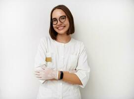 lächelnd jung weiblich Arzt Praktikant posieren mit gekreuzt Waffen gegen Weiß Hintergrund mit Kopieren Raum foto