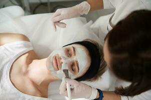 hoch Winkel Aussicht von ein Frau Empfang kosmetisch Verfahren im Spa Center. feuchtigkeitsspendend Gesicht Maske . Gesichts- Haut Behandlung. foto