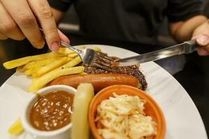 Mann Essen gegrillt Fleisch Anteil von Platte. Hand halten Messer und Gabel Schneiden gegrillt Rindfleisch Steak foto