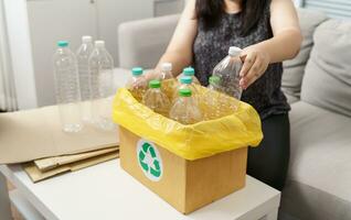 Zuhause recyceln Öko Grün Null Konzept Frau werfen leeren Plastik Flasche im Recycling Behälter mit Gelb Müll Taschen beim heim. foto