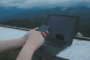 jung Geschäft Frau Arbeiten beim das Computer im Cafe auf das Felsen. jung Mädchen Herunterschalter Arbeiten beim ein Laptop beim Sonnenuntergang oder Sonnenaufgang auf das oben von das Berg zu das Meer, Arbeiten Tag. foto