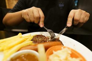 Mann Essen gegrillt Fleisch Anteil von Platte. Hand halten Messer und Gabel Schneiden gegrillt Rindfleisch Steak foto