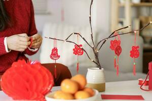 asiatisch Frau dekoriert Haus zum Chinesisch Neu Jahr Feierlichkeiten. Putten traditionell Anhänger zu das Chinesisch Mond- Neu Jahr zum gut Glück. Chinesisch Wort meint Segen foto