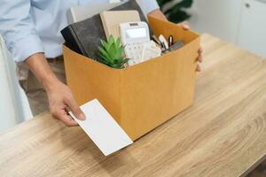 Senden Rücktritt Brief zu Boss und halten Zeug zurücktreten drücken oder Tragen Karton Box durch Schreibtisch im Büro foto